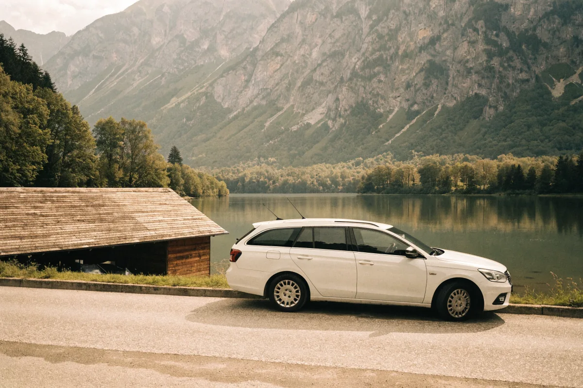 Weißer Kombi an einer Uferstraße im Salzkammergut, dahinter See und Bergkette