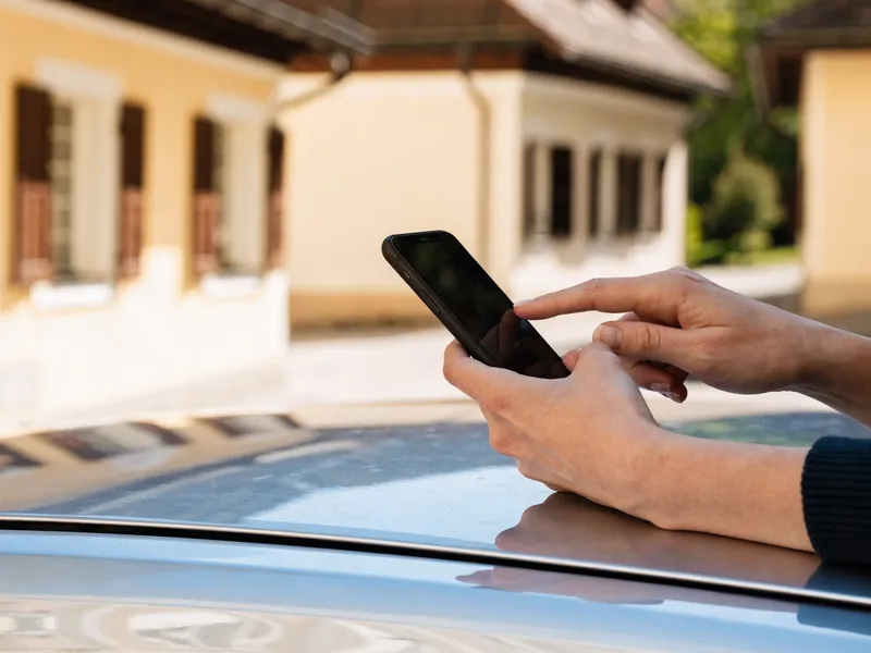 Hände geben die Fahrzeugdaten am Smartphone ein, aufgestützt auf ein Autodach