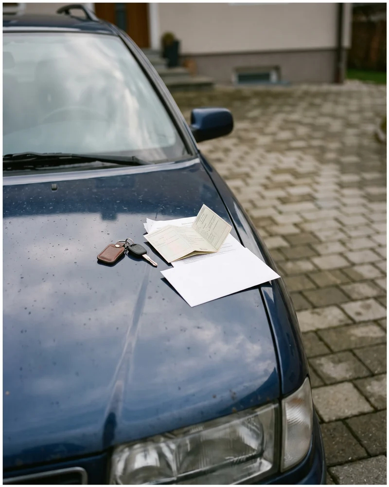 Autoschlüssel, Fahrzeugpapiere und ein Kuvert liegen auf der Motorhaube eines Kombis in einer Einfahrt